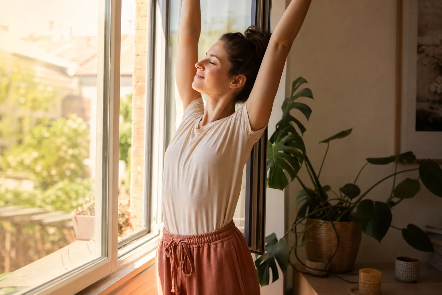 A woman stretching by an open window in bright morning light, smiling slightly